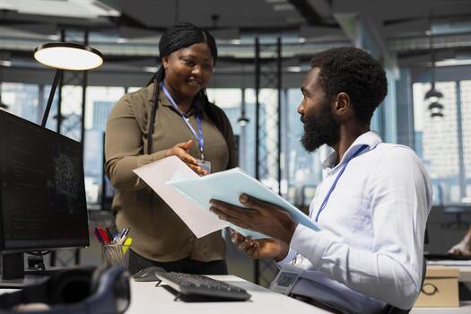 Manager in office handing paperwork to employee working with AI assistant on PC. Worker supervised by team leader while using artificial intelligence to streamline administrative tasks, camera A. photo