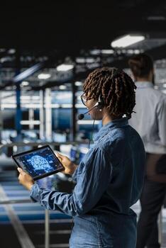 Server hub engineer uses tablet and headset mic to provide remote assistance on industrial platform in data center. Server room professional solves backend issues, coordinating remote teams. photo