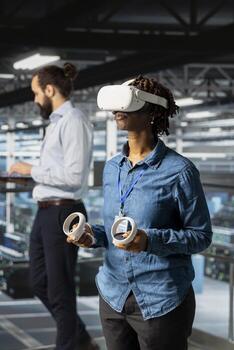 Woman engineer analyzing performance outputs using virtual reality tech on data center industrial platform. Server hub technician finetuning server rig configurations with VR headset. photo