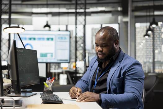 Black business consultant taking notes to create a new strategy and fulfill project goals in a modern office, writing some data insights to forecast a global expansion. Motivation for efficiency. photo