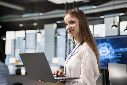 Smiling junior developer utilizing artificial intelligence to optimize performance using laptop. Cheerful young female engineer in office training machine learning models with notebook photo