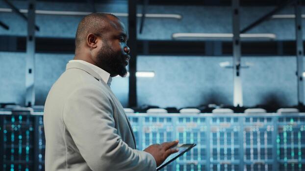 Technician working in high tech server hub, analyzing data on tablet to ensure seamless data flow. IT expert examining equipment in data center, ensuring system integrity and security, camera B photo