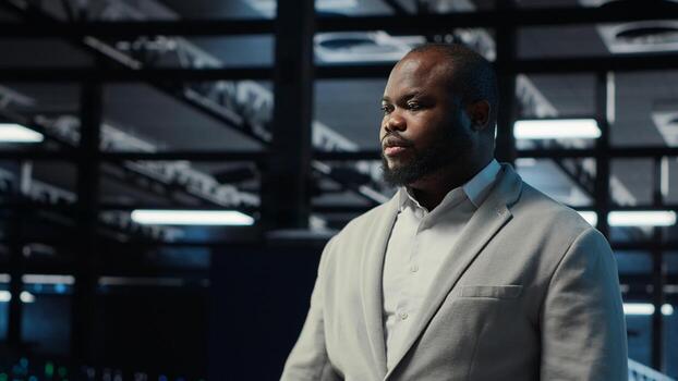 Admin working in high tech server hub capable of processing and storing vast amounts of data. African american IT specialist troubleshooting server rows controlling network resources, camera B photo