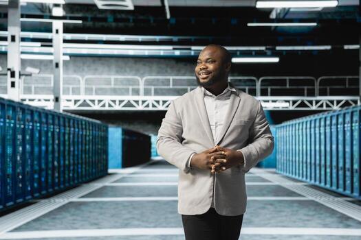 Smiling admin walking in server room, overseeing mainframes gear used for managing databases. Jolly IT specialist in data center workplace doing checkup on rackmounts storing information photo