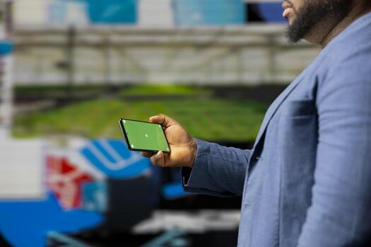 African American tech enthusiast looking at chroma key screen next to digital interfaces and multimedia visuals, showcasing content creation, mobile technology and global online influence. photo