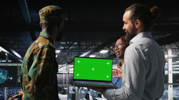 Military command center engineering team using chroma key notebook. Army IT expert and coworkers in data center using green screen laptop to defend networks against threats, photo