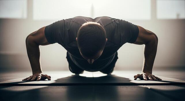 Determined man performing push-ups on a mat in a backlit gym setting. photo