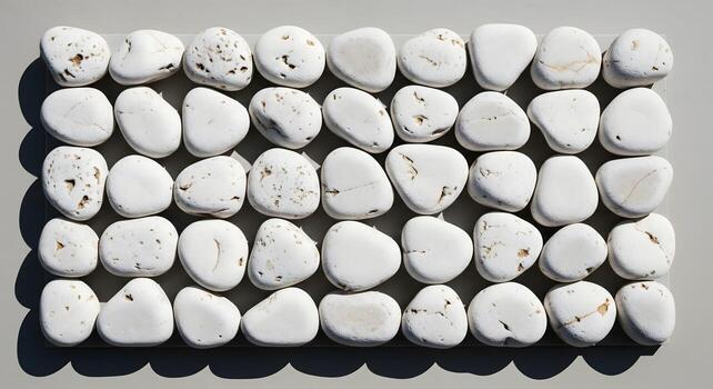 Top view of neatly arranged white pebbles in a grid pattern on a plain background, creating a calm and orderly texture photo