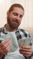 jung Mann prüft frisch Verdienste Gehalt beim heim, langsam Zählen jeder Geld Dollar Kasse Banknoten mit ein zufrieden Ausdruck. kaukasisch lächelnd Kerl Gefühl glücklich Über Mittel zum geteilt finanziell Tore video