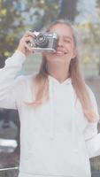 caucásico joven mujer turista de viaje en fines de semana explorador pueblo mirando ciudad papel mapa, haciendo foto imágenes en retro Clásico cámara al aire libre. contento adolescente niña viajero en urbano ciudad calle. video