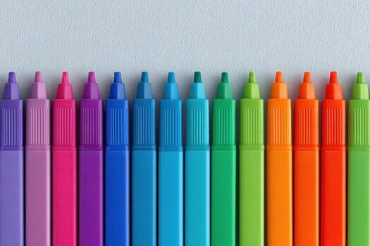 Marking pens in various vivid colors are neatly aligned on a light backdrop. The array transitions from purple through blue to green and orange, creating a striking visual effect. photo
