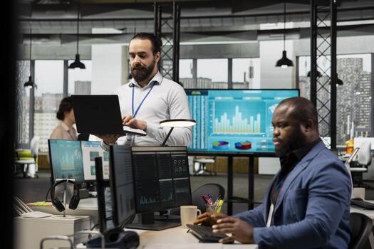 Male boss strategizes in a modern workplace surrounded by colleagues, utilizing data charts and graphs to generate detailed reports and statements that enhance business management. photo