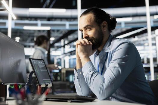 Data center software developer monitoring system performance using PC, identifying bottlenecks. Server farm IT specialist troubleshooting computer bugs, implementing optimizations photo