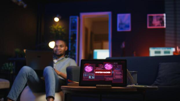 Black IT professional in loft working on cybersecurity with gadgets, tackling hacking attempts, encryption and cyber defense. Screen shows security breach warning, data security risks. Camera A. photo
