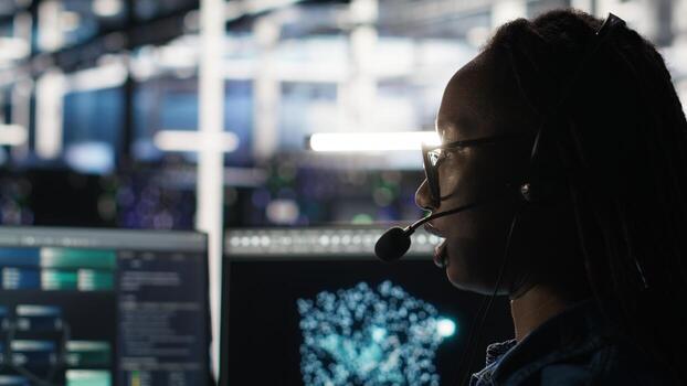 Data center employee uses audio headset and visual programming dashboard to troubleshoot client reported issues. Server farm technician looks at node tree interface, talking in microphone photo