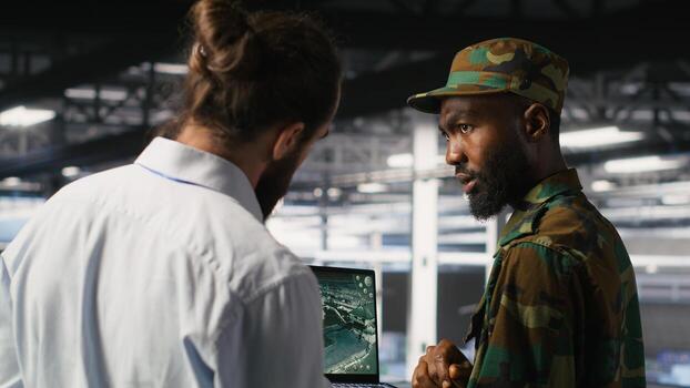 Military experts in data center reviewing drone surveillance feed on laptop screen. Army units in high tech server room doing battlefield reconnaissance operations using notebook photo