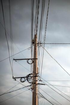 Tangled Wires On A Concrete Pole. A low-angle shot of a concrete utility pole with a chaotic tangle of electrical and communication wires against a cloudy sky. photo