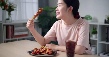 portátil tomada, ásia mulher desfrutando delicioso churrasco dentro vivo quarto às lar. caseiro Comida. comendo com relaxamento video