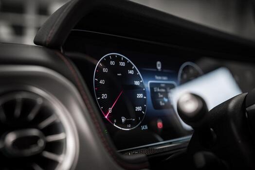 Close up view of a car dashboard featuring a digital speedometer, red stitched trim, metallic air vent, and high resolution displays indoors. photo