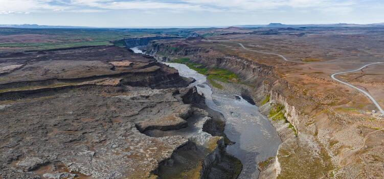 Aerial view of Studlagil Canyon in Iceland, featuring basalt columns, a winding river, steep cliffs, and a road running parallel to the rugged terrain. photo