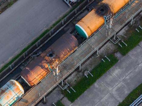 Aerial view of colorful and rusted tanker railcars on parallel tracks in Riga, Latvia, bordered by a road and grassy patches with visible infrastructure. photo