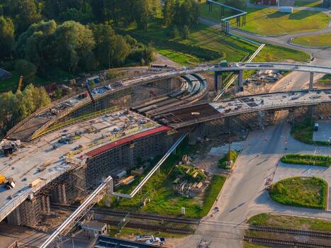 Aerial view of a multi level bridge under construction in Riga, Latvia, with curved roadways, scaffolding, green spaces, and railway tracks below. photo