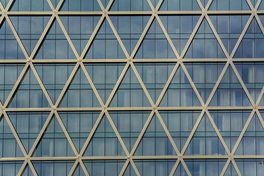 A building facade features a repeating pattern of triangular metal beams filled with reflective glass. The modern lattice design combines structural precision with visual rhythm. photo