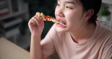 palmare alto angolo Visualizza sparo, rilassato asiatico donna godendo mangiare grigliato barbecue al chiuso, guardare contento e rilassato. fatti in casa cibo. video
