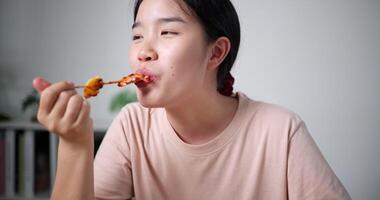 allegro asiatico donna godere mangiare delizioso fatti in casa barbecue spiedini su tavolo cenare nel vivente camera. fatti in casa cibo. mangiare con rilassamento video