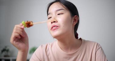 rilassato asiatico donna godendo mangiare grigliato barbecue al chiuso, guardare contento e rilassato. fatti in casa cibo. video