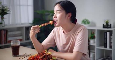 palmare sparo, rilassato asiatico donna godere mangiare grigliato barbecue al chiuso, guardare contento e rilassato. fatti in casa cibo. video