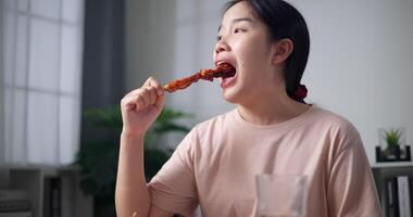 palmare Basso angolo Visualizza sparo, asiatico donna mangiare barbecue su cenare tavolo nel accogliente vivente camera. fatti in casa cibo. rilassante cenare a casa. video