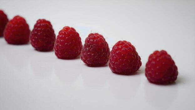 six fresh raspberries arranged in a row on a white background. The berries are bright red and juicy, creating a feeling of naturalness and freshness. photo
