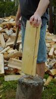A man is trying to split a log into firewood using an axe, against the backdrop of a pile of wood. Slow motion. Vertical. video