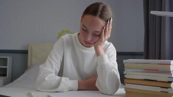 esausto alunno guardare annoiato e stanco mentre studiando a sua scrivania con un' mucchio di libri e un' computer portatile, lottando con concentrazione e motivazione video