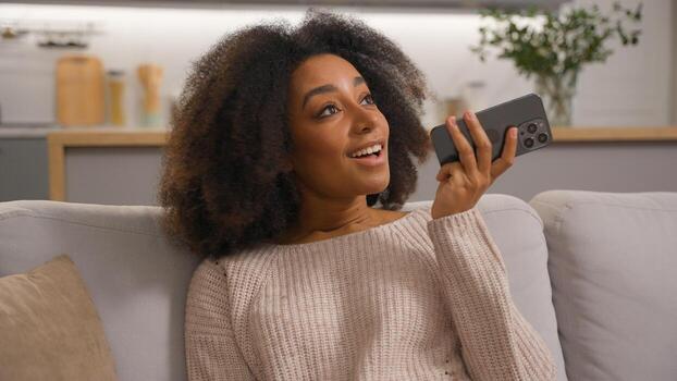 Positive African American woman recording audio message using easy command mobile application assistance talk at phone smiling female girl record voice mail using speakerphone convenient usage at home photo