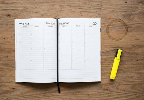 Flat lay composition of opened weekly planner with visible coffee cup ring and highlighter placed on rustic desk surface, no hands present photo
