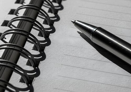 Macro close-up image of textured spiral notebook with metallic pen lying diagonally across, crisp paper grain and clean shadows photo
