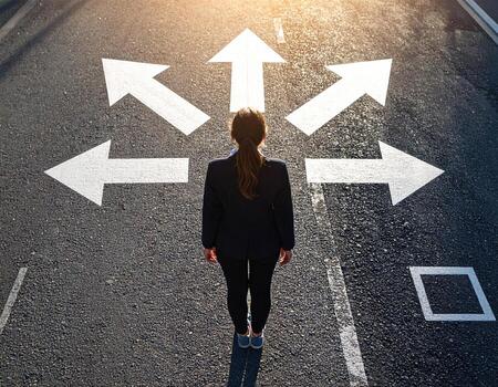 A woman in a business suit standing in the middle of an intersection with arrows pointing in different directions photo