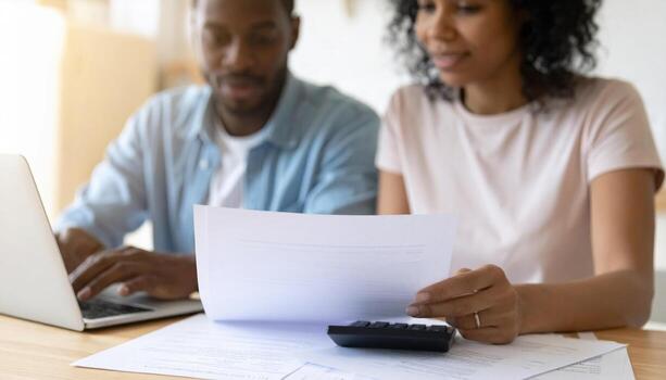 Couple reviewing financial documents together at table with calculator and laptop, creating productive atmosphere photo