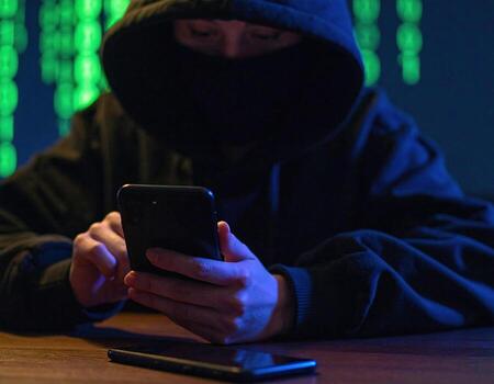Hooded figure types rapidly on smartphone, surrounded by digital green matrix backdrop, creating atmosphere of mystery and intrigue. glow from device highlights intense focus of individual photo