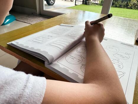 A young student sits at a wooden desk working on basic math exercises, steadily developing essential problem solving skills.d photo