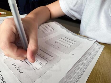 A young student sits at a wooden desk working on basic math exercises, steadily developing essential problem solving skills.f photo