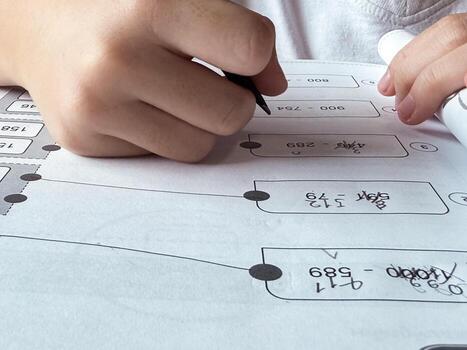 A young student sits at a wooden desk working on basic math exercises, steadily developing essential problem solving skills.r photo