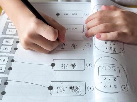 A young student sits at a wooden desk working on basic math exercises, steadily developing essential problem solving skills.c photo