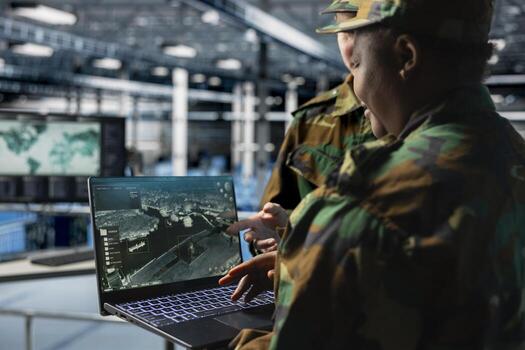Team of army experts in data center reviewing satellite intelligence feeds on laptop. Military units in server farm command center supporting battlefield strategy with orbital imaging analysis photo