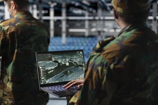 Close up of army specialist in data center scanning terrain after enemy lines using military satellite control. Soldier wearing uniform in server room managing orbital telemetry on notebook photo