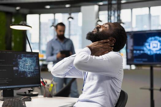 cansado ingeniero en oficina relajante rígido cuello mientras utilizando ai herramientas a automatizar rutina codificación tareas. fatigado eso experto masajear cuello a eliminar dolor, utilizando artificial inteligencia a hacer desarrollo foto