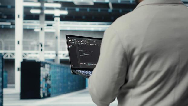 Engineer walking in data center using device to configure hardware optimized for AI tasks. Man doing maintenance on rigs performing load balancing for artificial intelligence computing, camera B photo