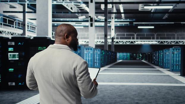 Admin walking in high tech data center facility, checking equipment for system stability. IT specialist overseeing server room, configuring supercomputers, optimizing performance, camera A photo